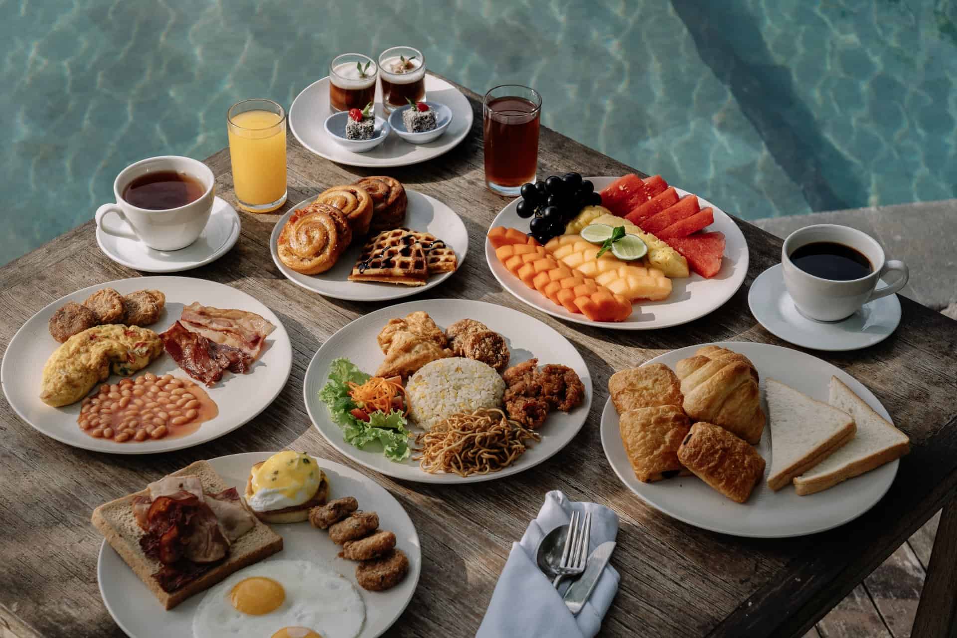 Poolside breakfast spread at Astagina Resort Legian, featuring fresh fruits, pastries, and hot dishes included in accommodation deals.