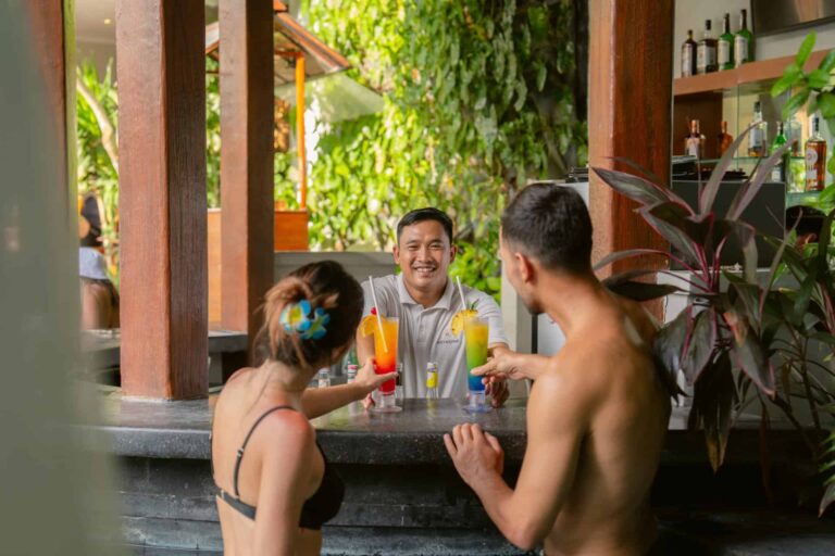 Guests enjoying cocktails at the pool bar of Astagina Resort Legian, highlighting relaxed resort facilities and added stay value.