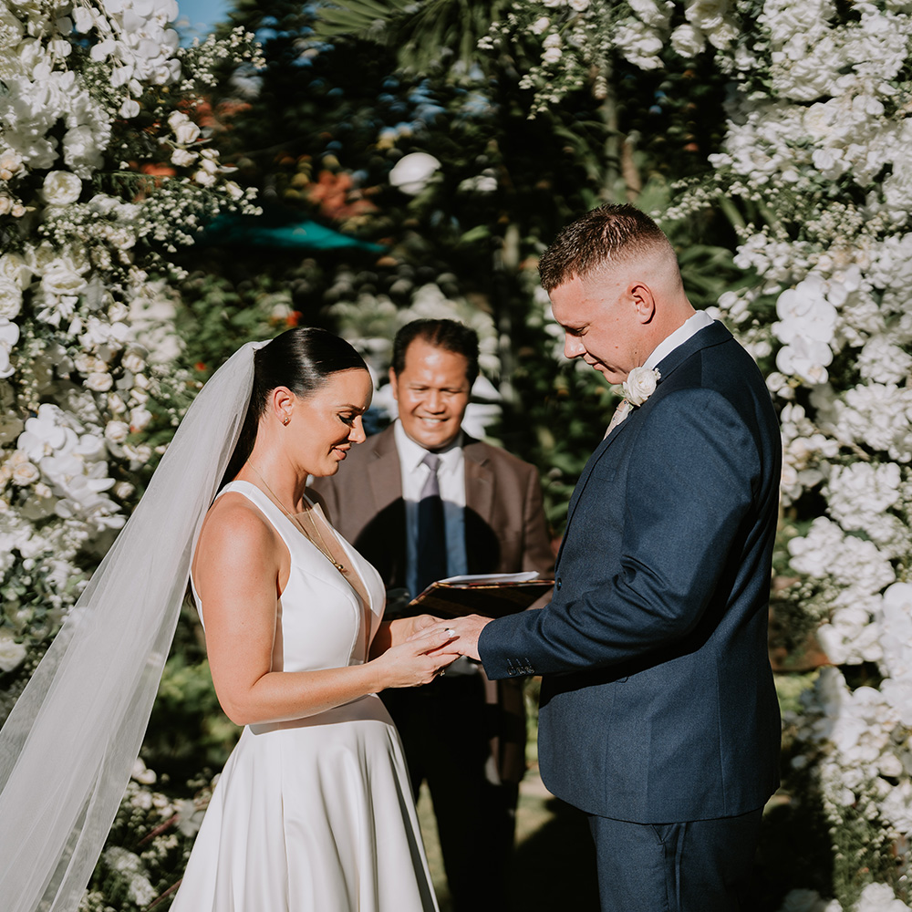 Bride and groom exchanging vows under a white floral arch during an intimate garden wedding ceremony at Astagina Resort Villa & Spa Legian in Legian Bali