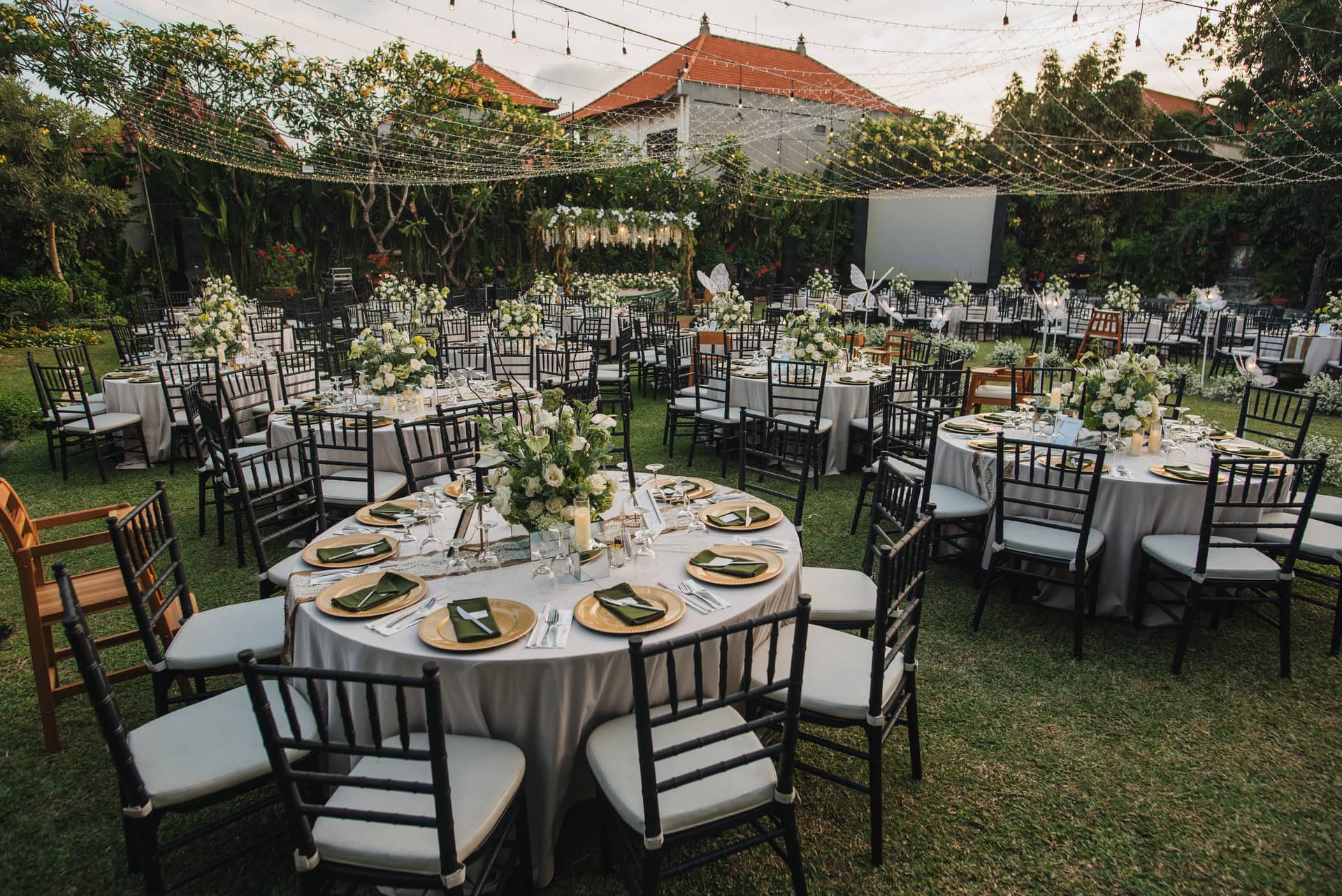 Spacious outdoor garden wedding reception at Astagina Courtyard featuring round table layout, floral centerpieces, ambient string lights, and tropical garden setting at Astagina Resort Villa and Spa Legian