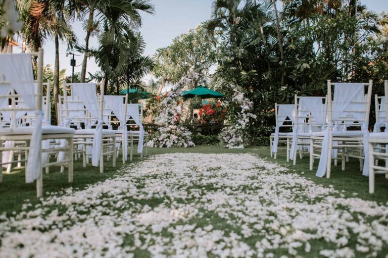 Garden wedding ceremony setup with white chairs, floral arch, and petal aisle at a Bali garden wedding venue in Astagina Resort Villa & Spa Legian
