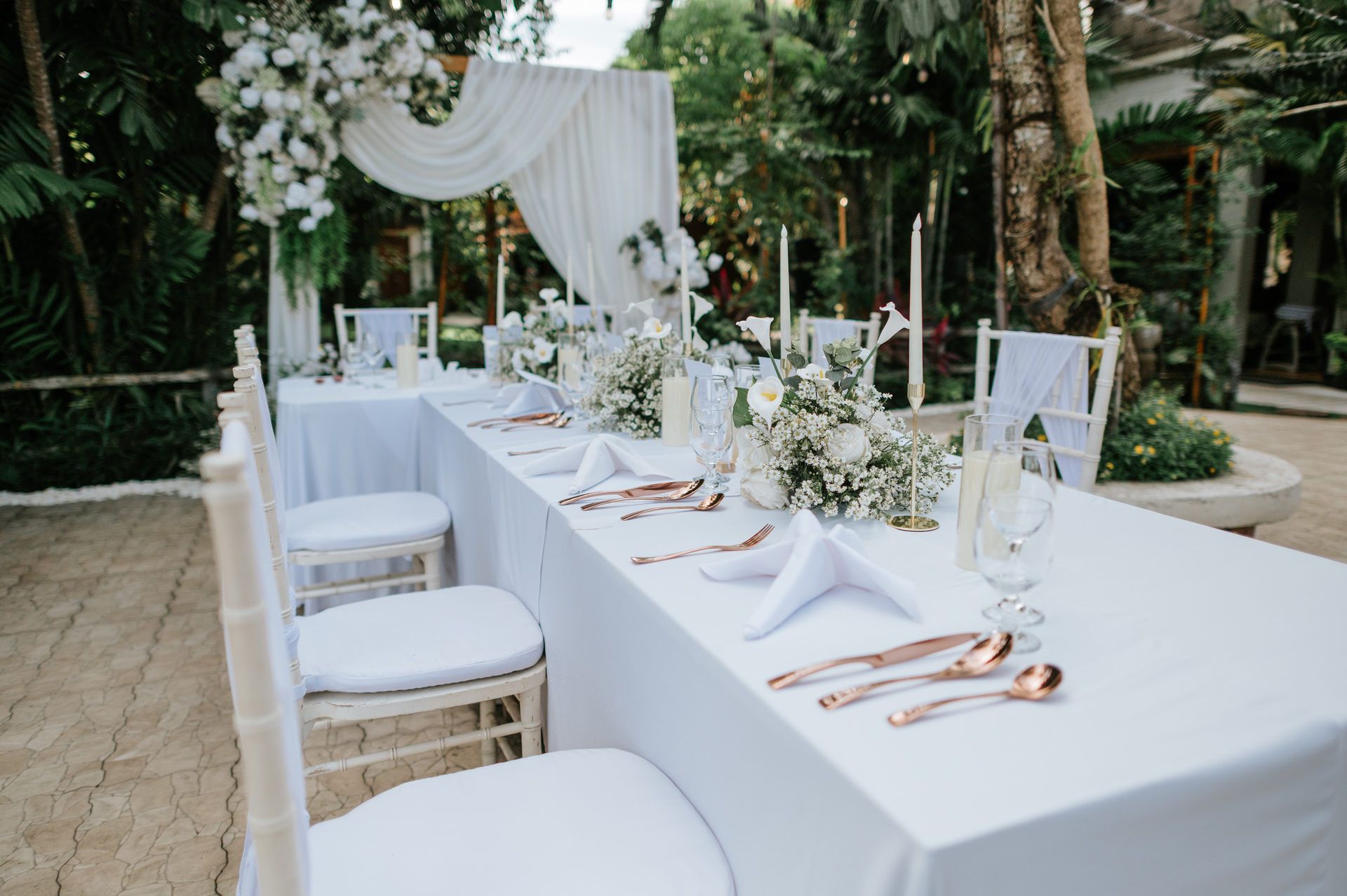 Intimate garden wedding dinner setup at Lagoon Lounge Astagina Resort with long table styling, white floral arrangements, candles, and draped backdrop for small Bali garden wedding celebration