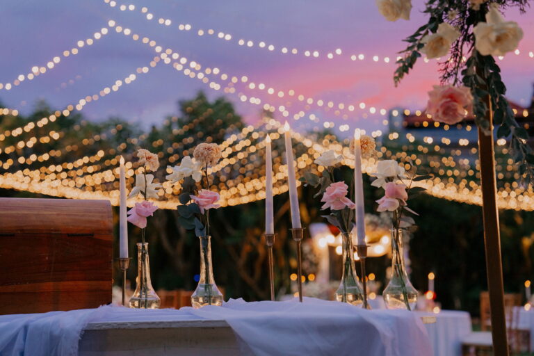 Elegant garden wedding reception setup in Bali with candles, floral arrangements, and string lights at sunset in Legian
